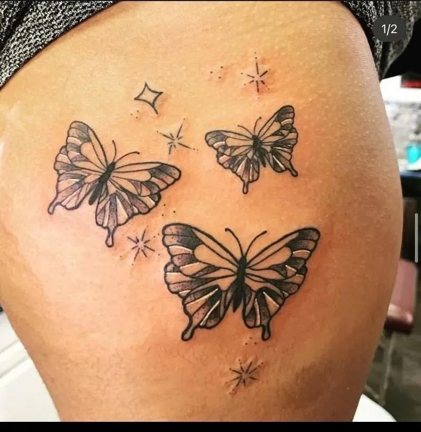 Three butterfly tattoos on the side of a person's hip, with small star and diamond accents.