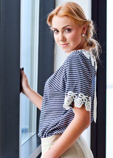 A woman in a striped shirt is standing next to a window.