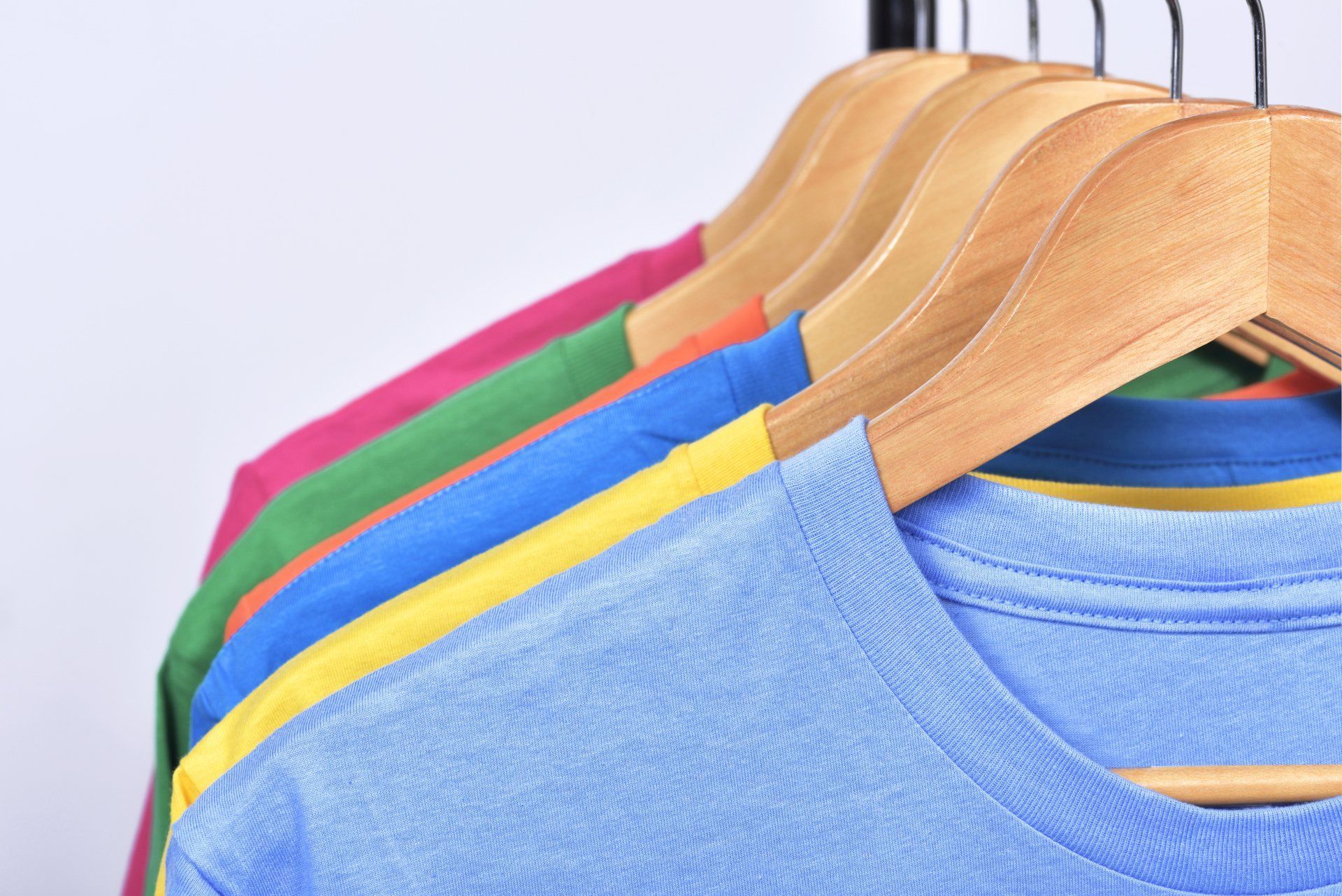 A row of colorful t-shirts are hanging on wooden hangers.