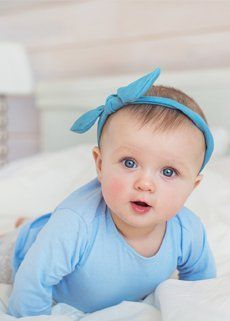 A baby wearing a blue headband is crawling on a bed.