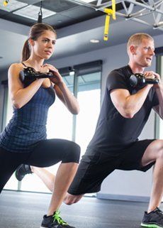 A man and a woman are doing squats with kettlebells in a gym.