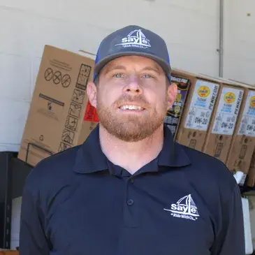 Man in a cap and polo shirt smiles in front of boxes; the cap and shirt have the name 