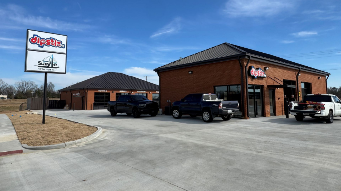 Gas station with a red and white canopy, a blue truck with a trailer, and a tire shop.