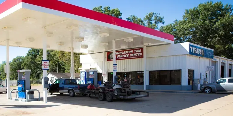 Gas station with a red and white canopy, a blue truck with a trailer, and a tire shop.