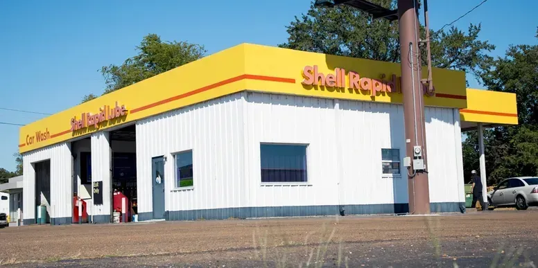 Shell gas station with car wash and yellow awning against a blue sky.