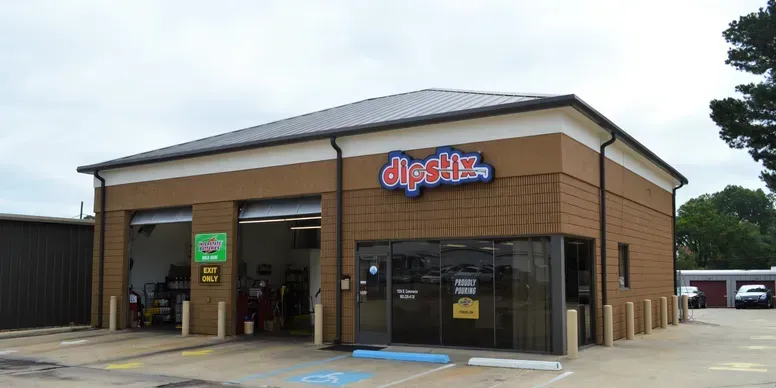 A brown DipStix auto shop with two garage bays open, under a cloudy sky.