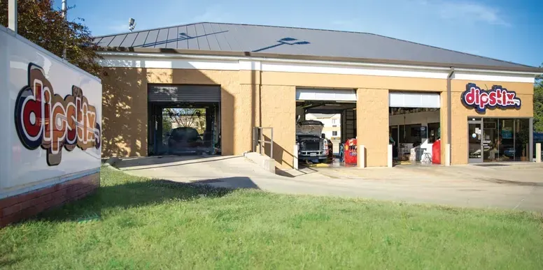 Exterior view of a Dipstix oil change shop with service bays and a large sign, set against a green lawn.