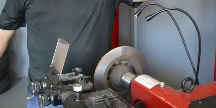 A person is machining a brake rotor on a lathe. Black shirt, red machine, silver rotor.