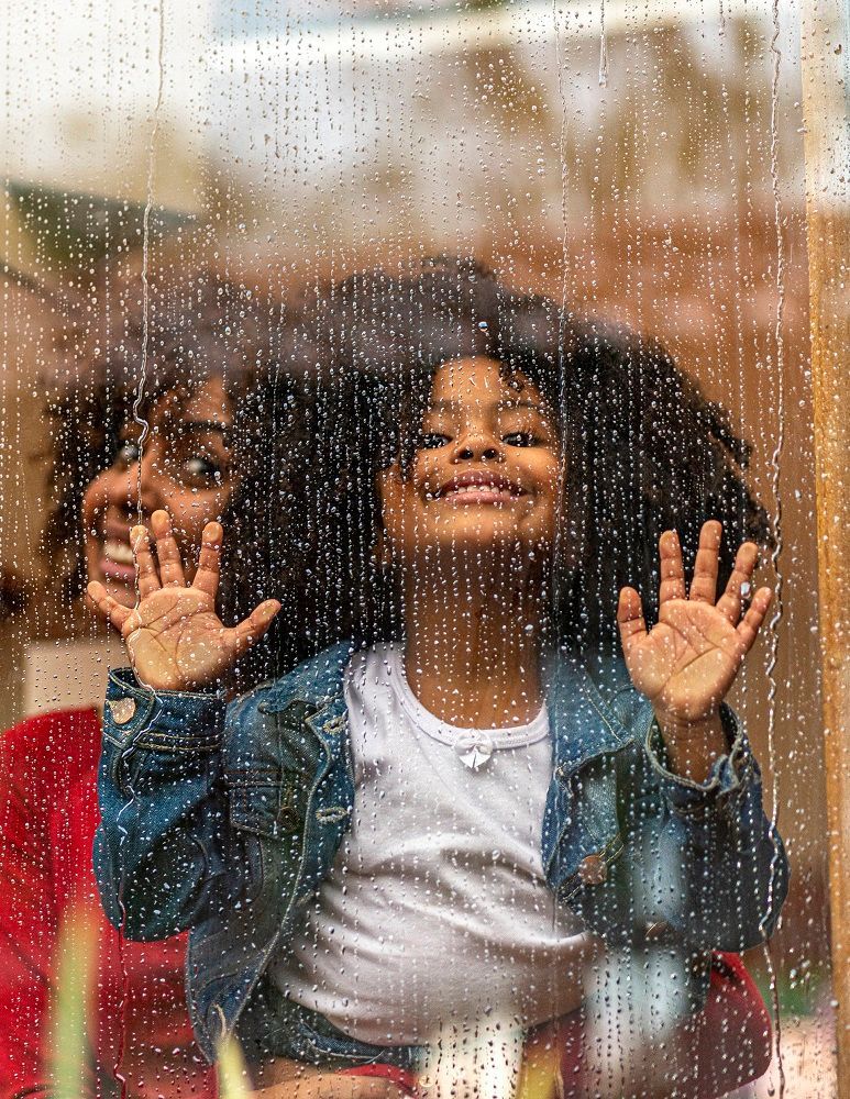 A child and adult smile, touching a window covered in raindrops.