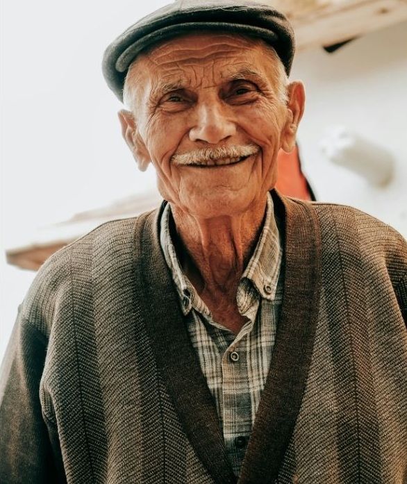 Smiling older person wearing a cap and sweater.