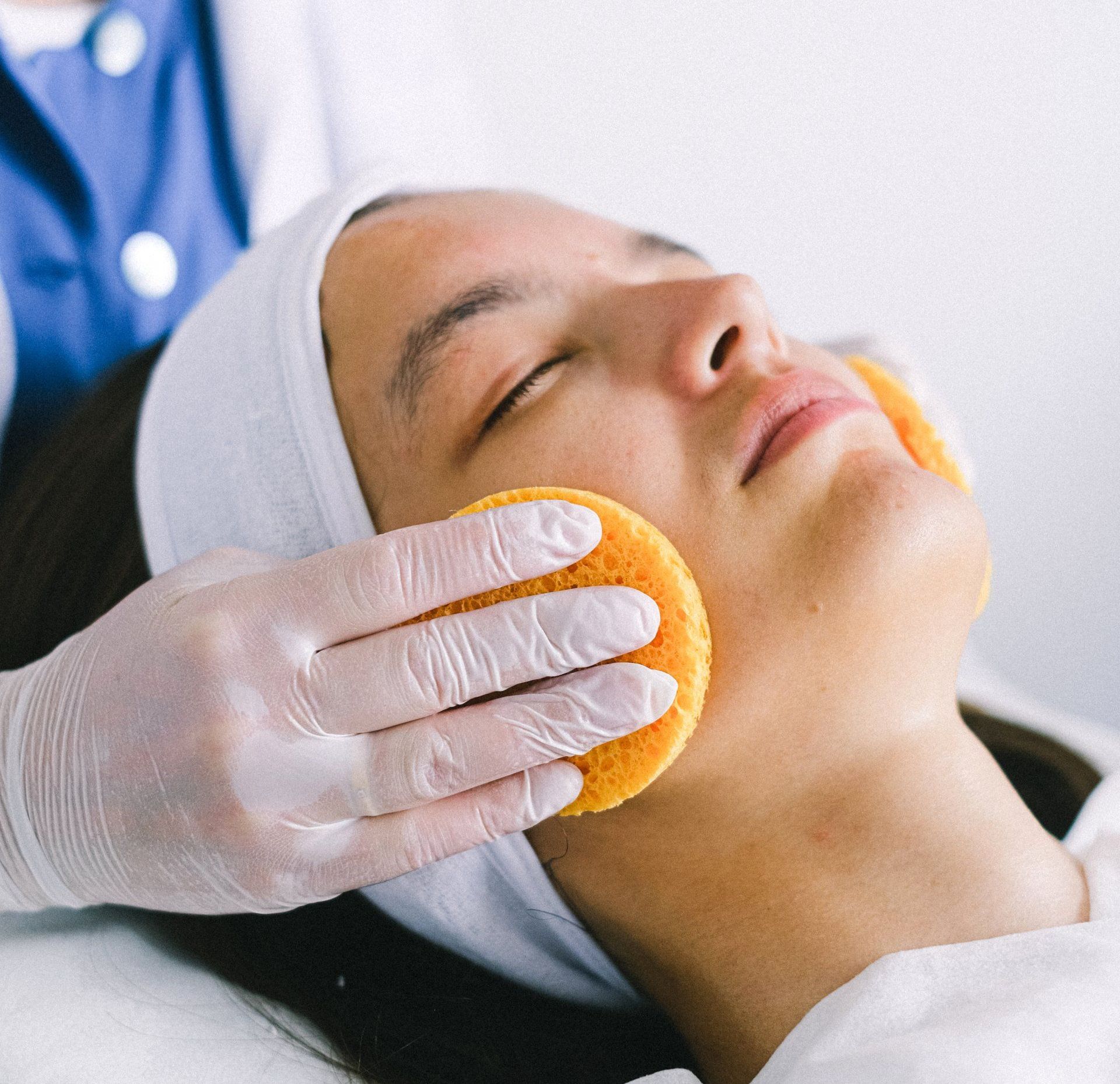 applying round yellow sponges on each cheek with latex gloves during European Facial