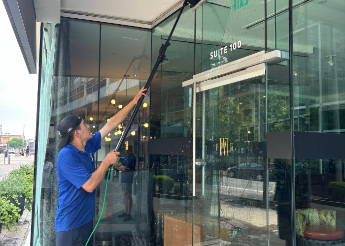 A man is cleaning a glass door with a hose.