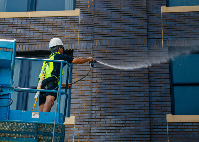 A man is cleaning a brick building with a high pressure washer.