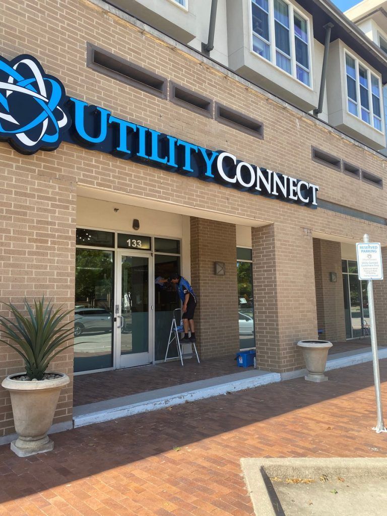 A man on a ladder is working on a sign for utility connect