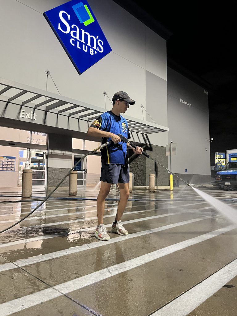 A man is using a high pressure washer to clean the outside of a sam 's club store.