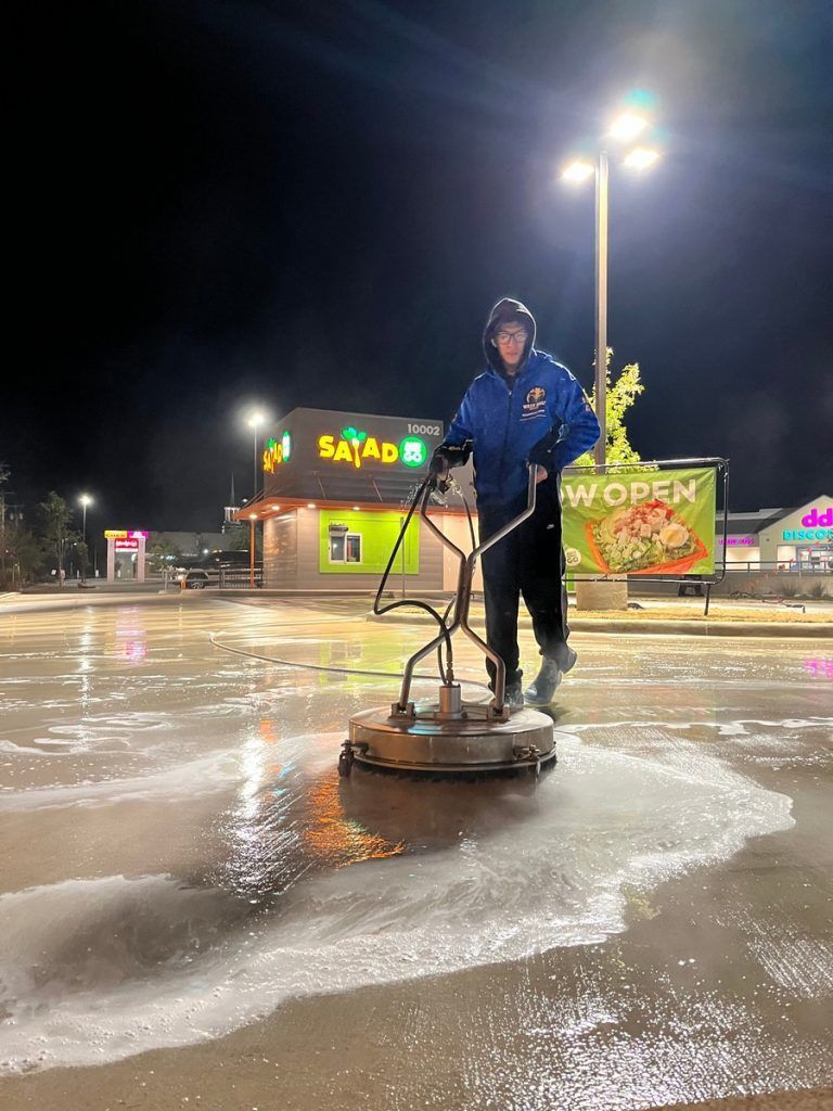 A man is using a machine to clean a parking lot at night.