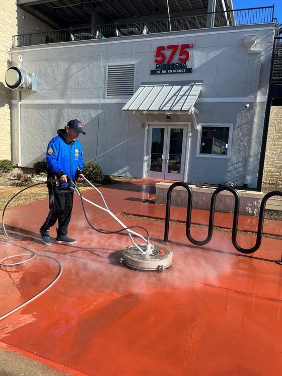 A man is cleaning a red concrete driveway in front of a building.