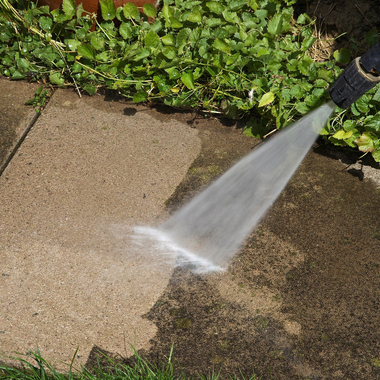 A person is using a high pressure washer to clean a sidewalk.