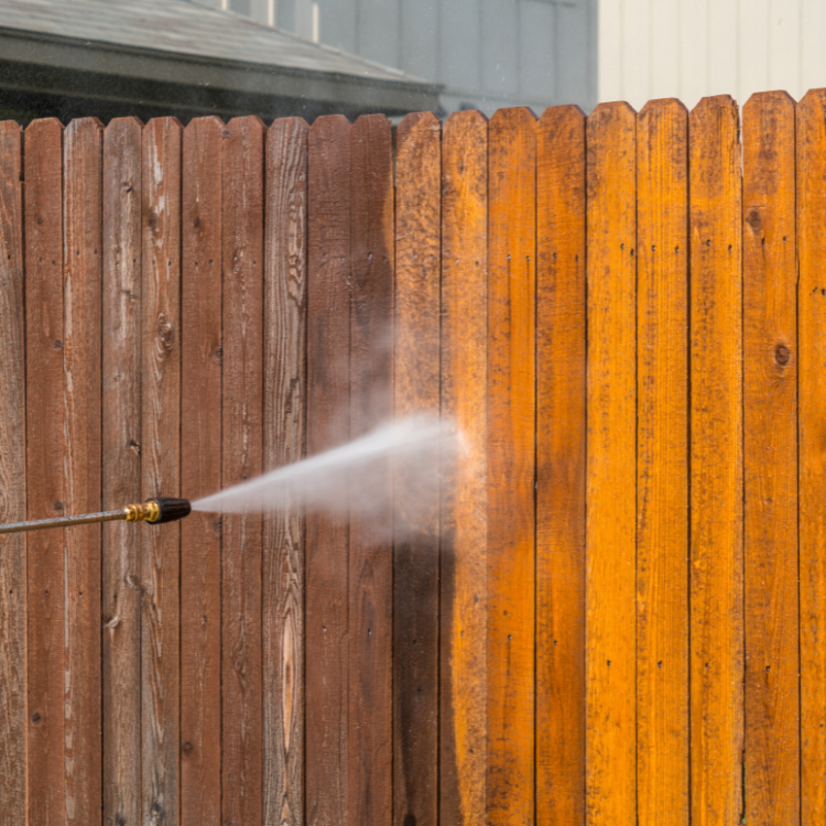 A person is using a high pressure washer to clean a wooden fence.