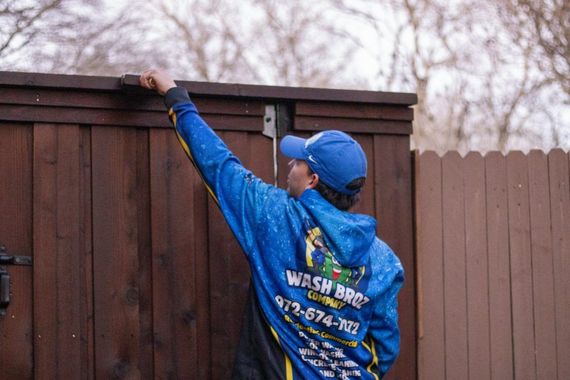 A man in a blue jacket is painting a wooden fence.