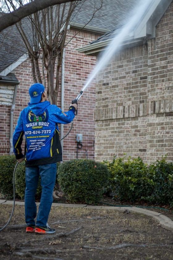 A man is cleaning the side of a brick house with a pressure washer.