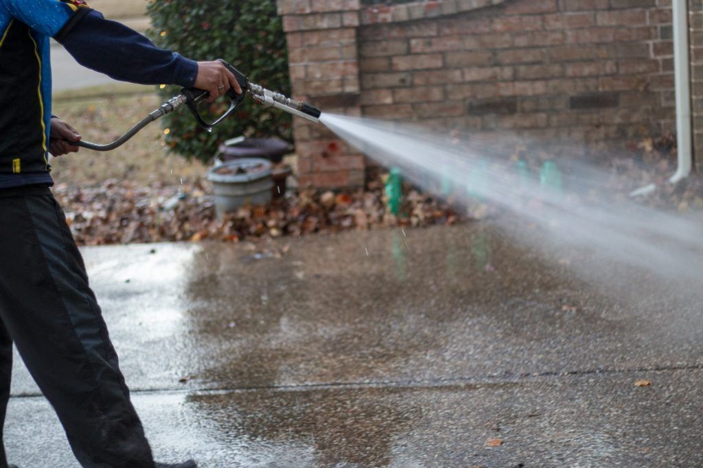 A man is using a high pressure washer to clean a driveway.