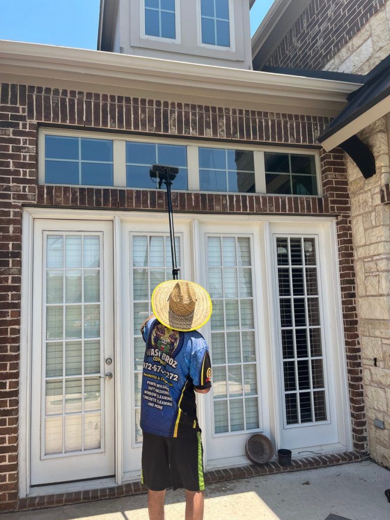 A man in a cowboy hat is cleaning the windows of a house.