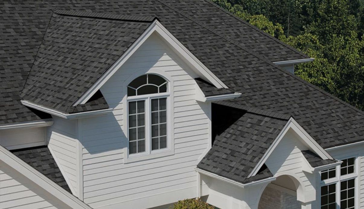White house with dark gray asphalt shingle roof, dormer with arched window.