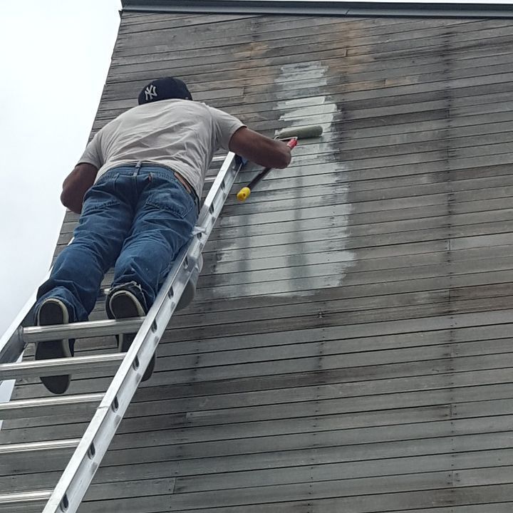 A man is painting a roof with a roller on a ladder.