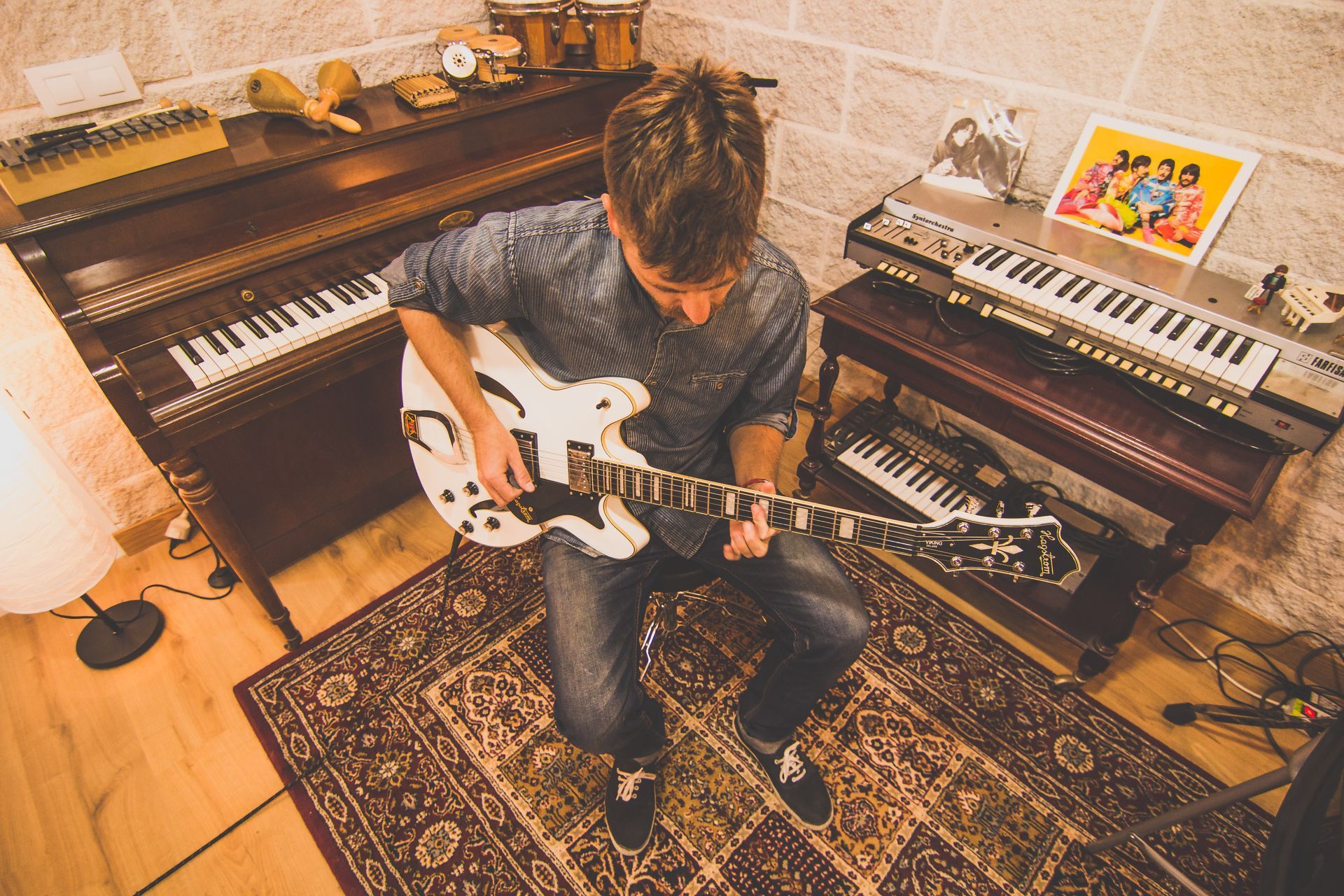 Un hombre está tocando una guitarra en una habitación con un piano y teclados.