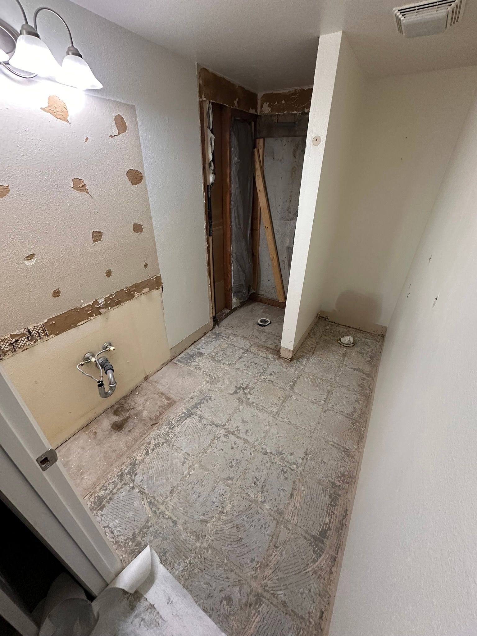 Bathroom undergoing renovation with exposed walls, subfloor, and plumbing fixtures.