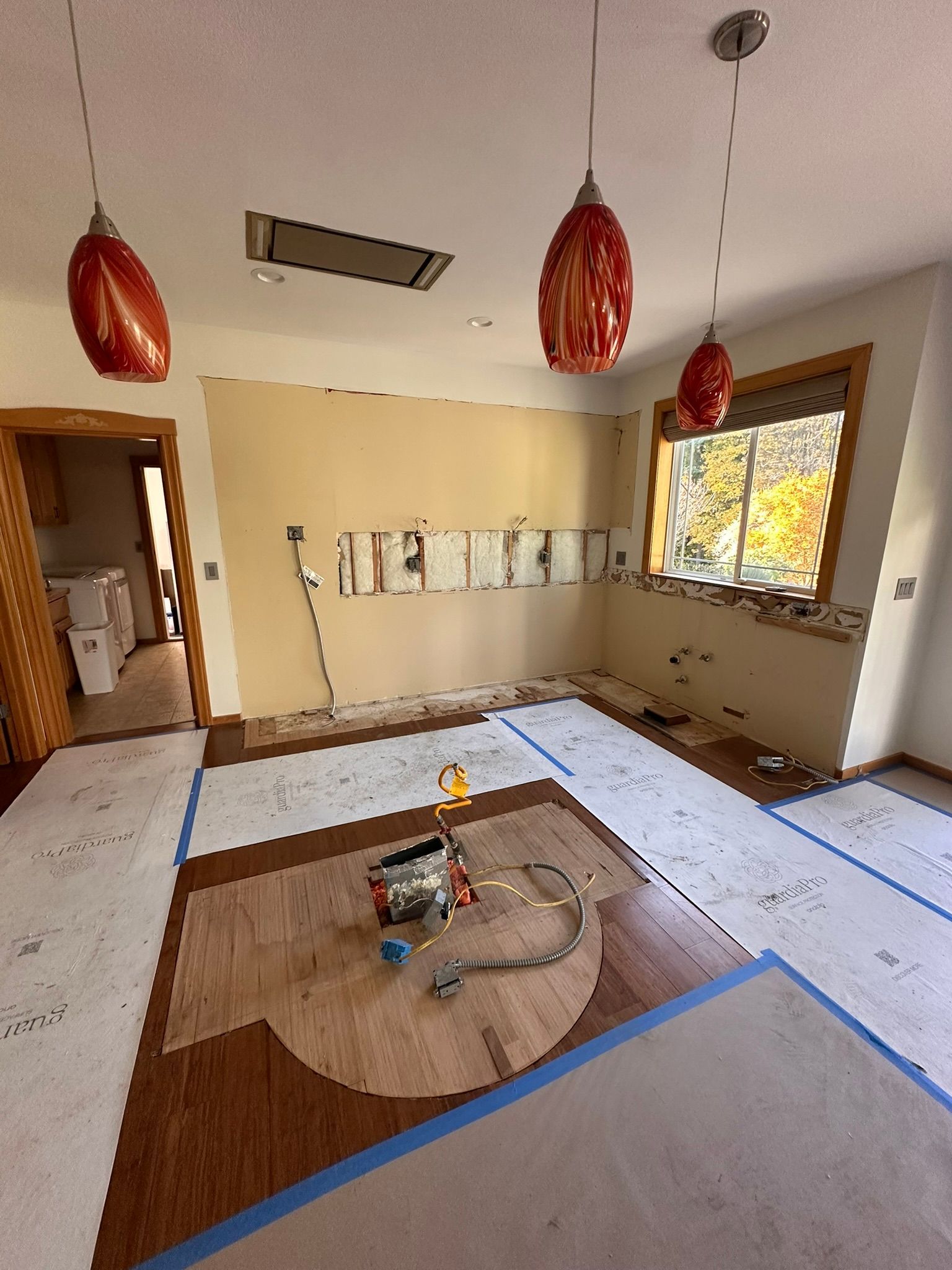Room under renovation with exposed wall, hardwood floor, red pendant lights.
