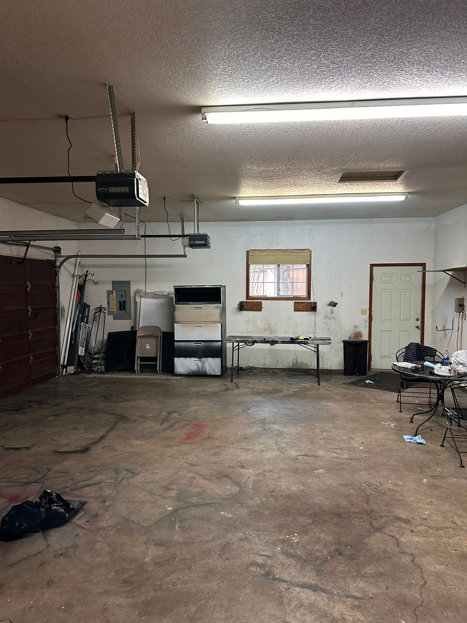 Empty garage with concrete floor and cluttered walls.  An overhead garage door is visible, and the room contains furniture.