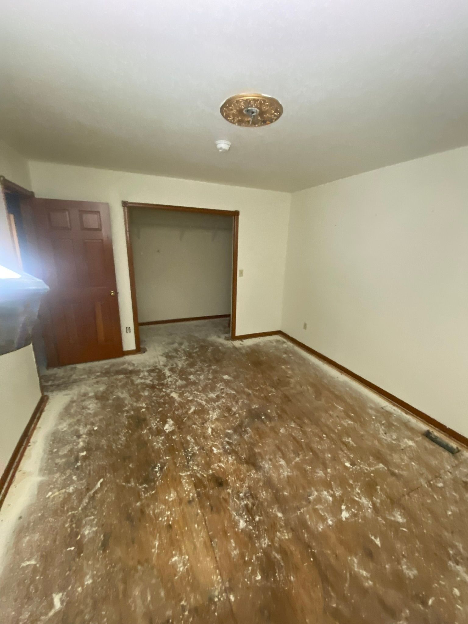 A room with exposed wood flooring covered in debris, a door, and an open doorway.