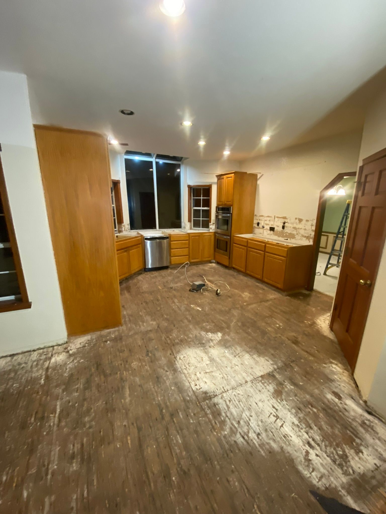 Kitchen undergoing renovation; cabinets installed, floor ripped up, debris visible, overhead lights.