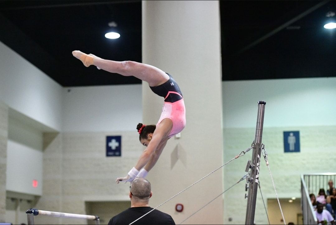 A female gymnast is doing a handstand on a parallel bars