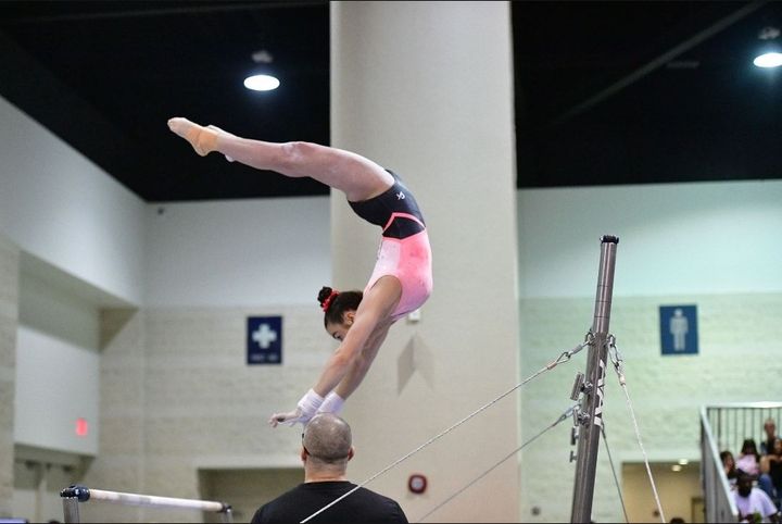 A female gymnast is doing a handstand on a parallel bars