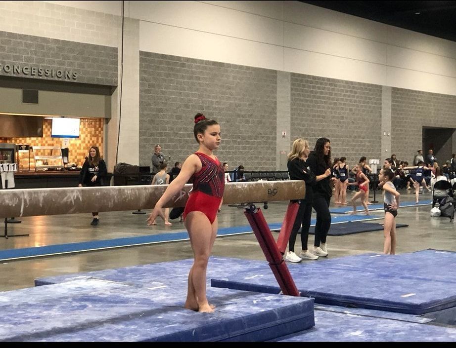 A young girl is standing on a balance beam in a gym.