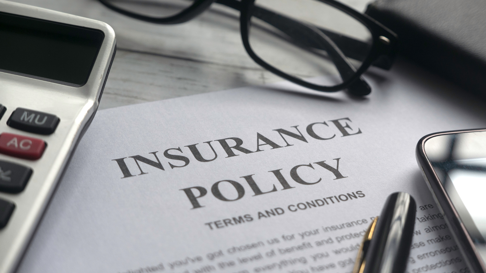 An insurance policy is sitting on a table next to a calculator and glasses.