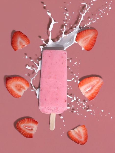 Glace à la fraise rose avec éclaboussures de lait et tranches de fraise sur fond rose.