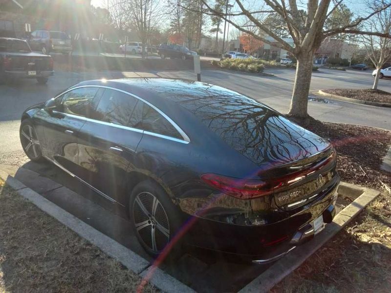 A black car is parked in a parking lot next to a tree.