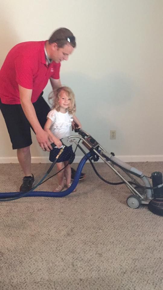 A man and a little girl are standing next to a vacuum cleaner.