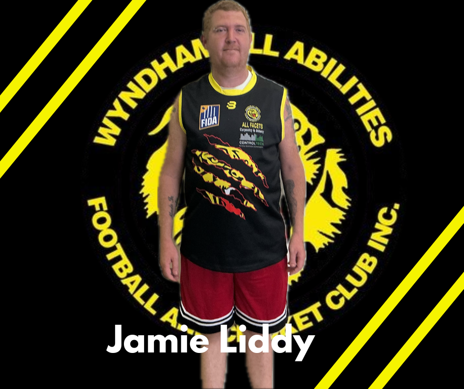 Jamie Liddy wearing a black Wyndham All Abilities football jersey and red shorts against a branded club logo backdrop.
