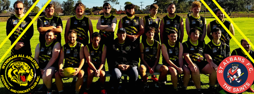 A large team of Australian rules football players in black and yellow uniforms pose for a photo on a grassy field.