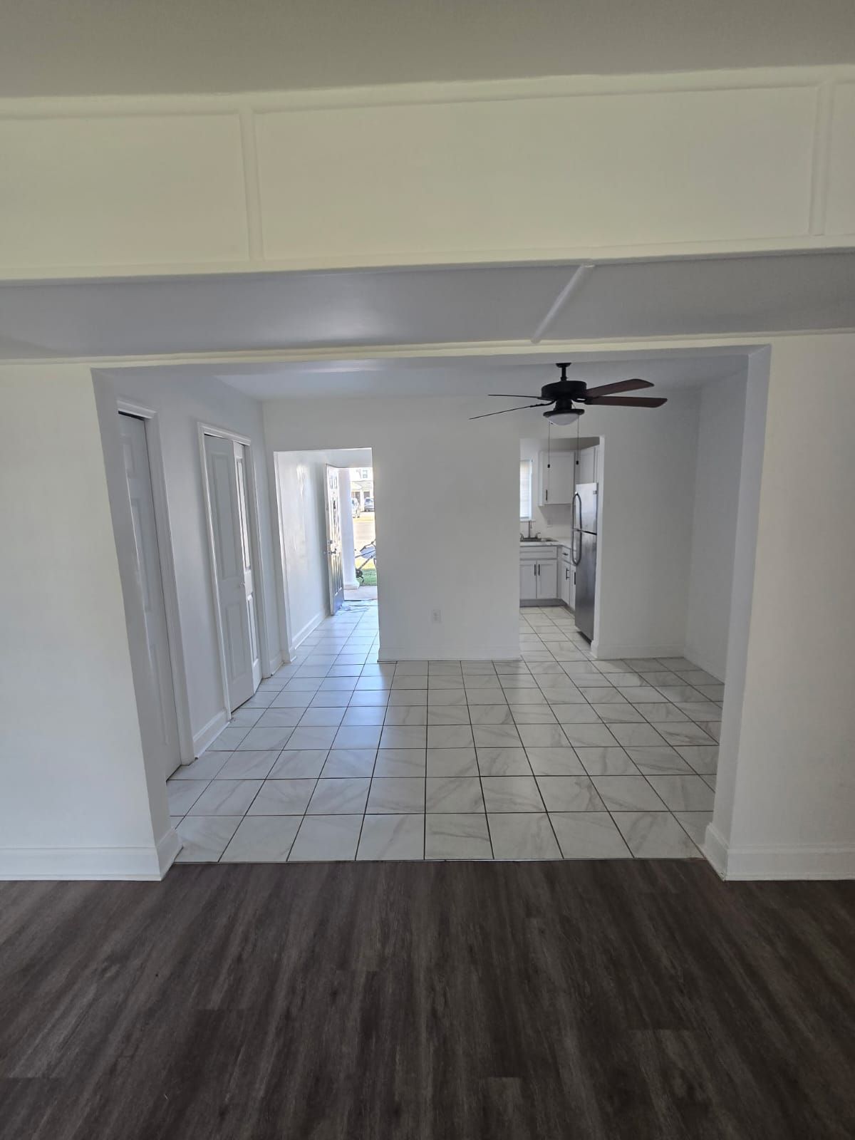 Living room with view into kitchen area featuring ceiling fan and natural light at Chateau Apartments Burlington, NJ