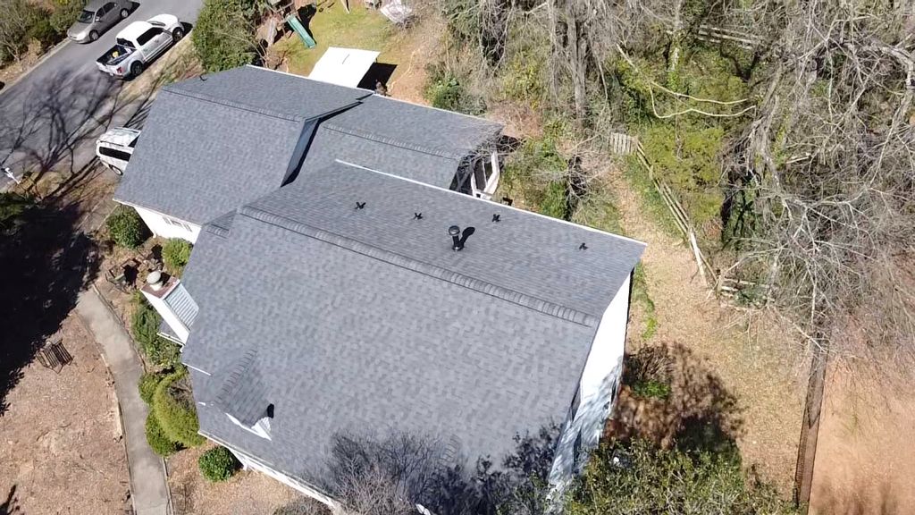 An aerial view of a house with a roof in the middle of a forest.