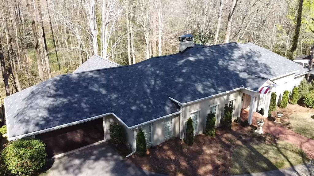 An aerial view of a house with a black roof surrounded by trees.