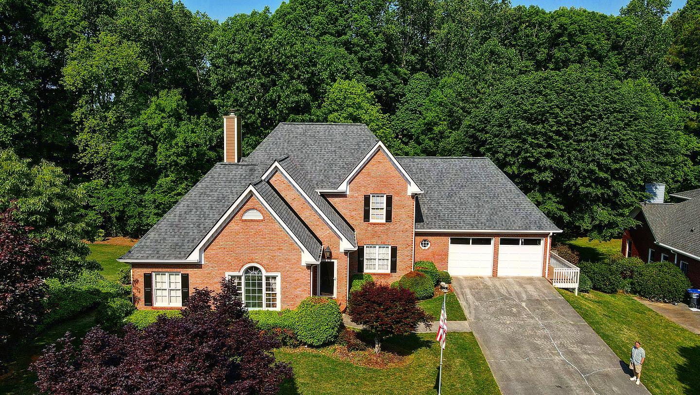 An aerial view of a large brick house with a gray roof surrounded by trees.