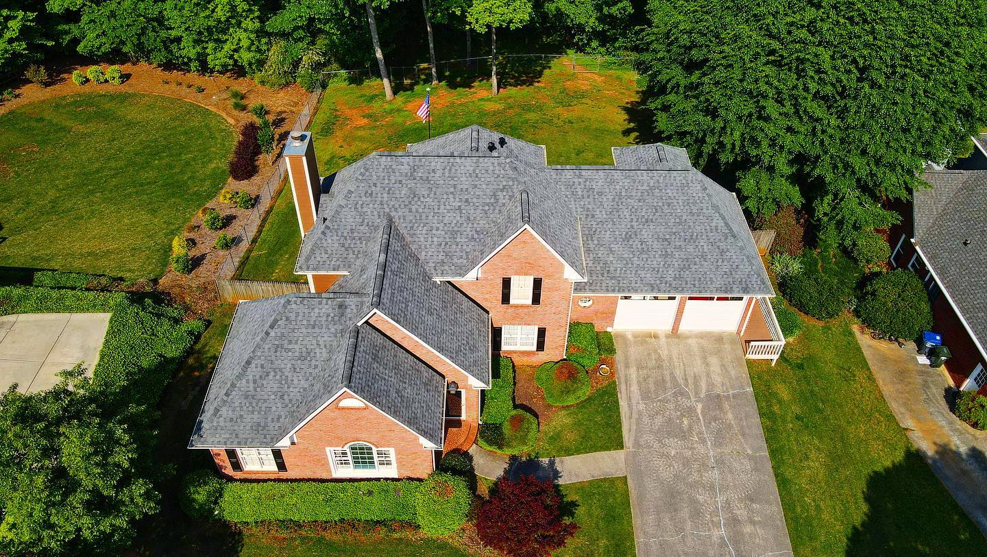 An aerial view of a large brick house with a gray roof surrounded by trees.