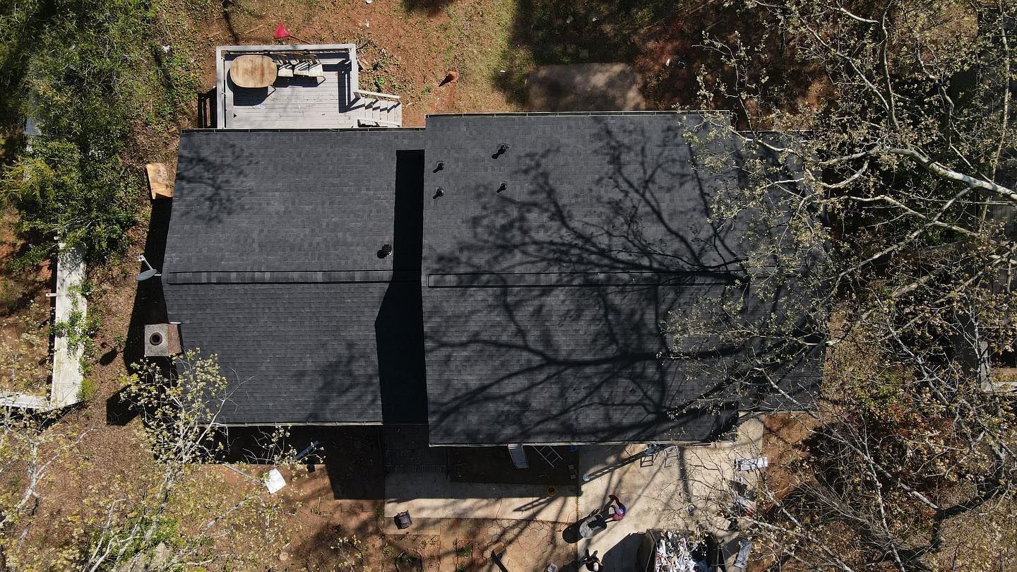 An aerial view of a house with a black roof surrounded by trees.